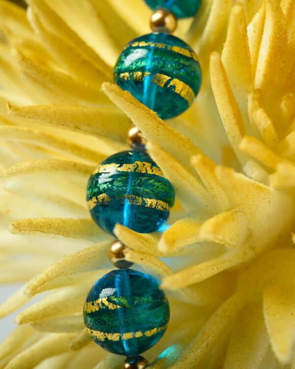 Close-up of a Murano necklace with vibrant blue and green beads featuring gold accents, displayed on a yellow decorative piece